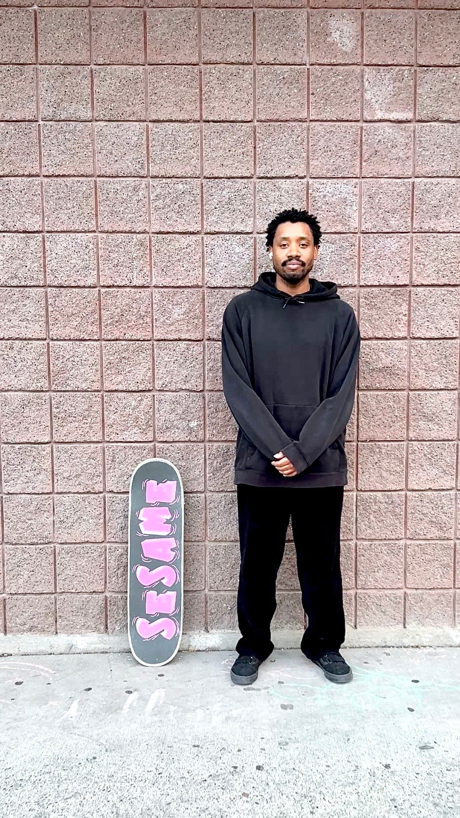 Joseph McGee standing beside a skateboard against a brick wall.