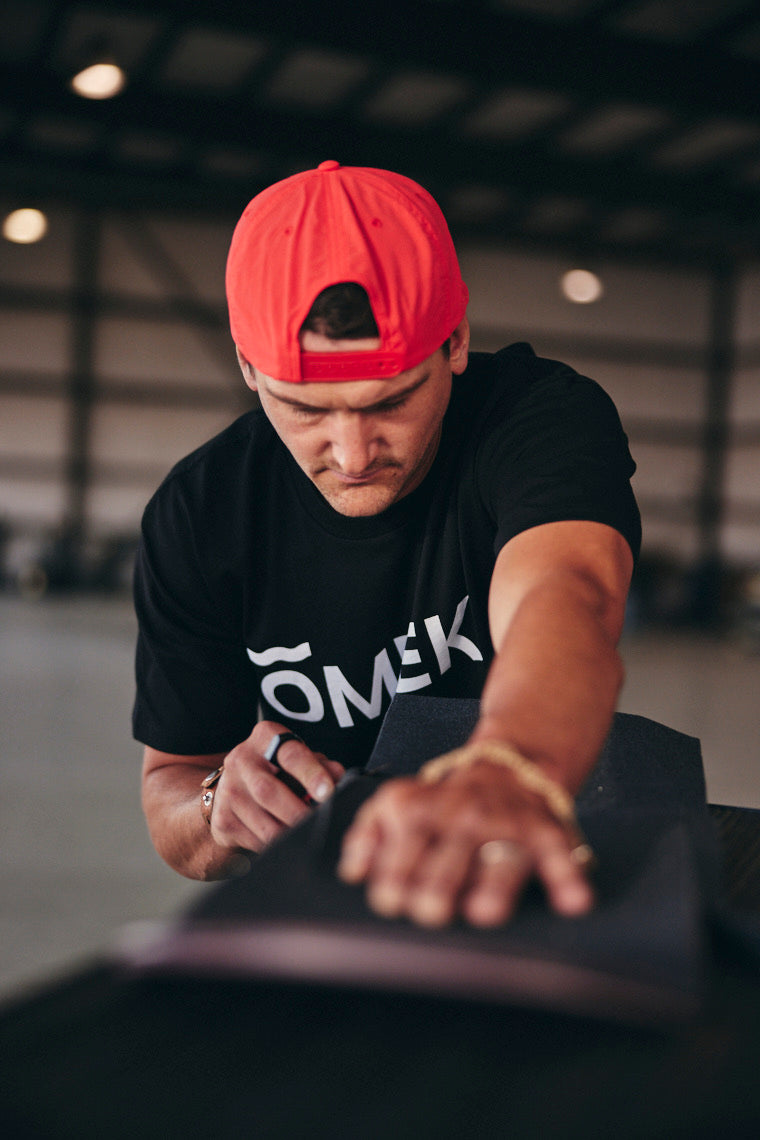 Kam Atwood in a red cap and black OMEEK shirt leaning over a ramp.
