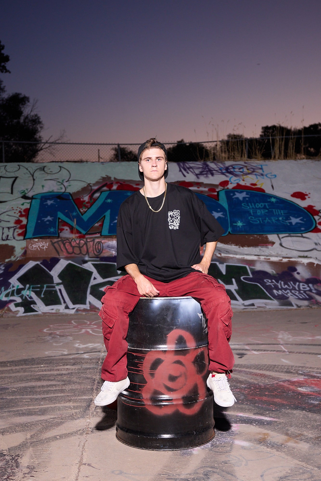Parker DeMoux sitting on a painted barrel in front of a graffiti wall.
