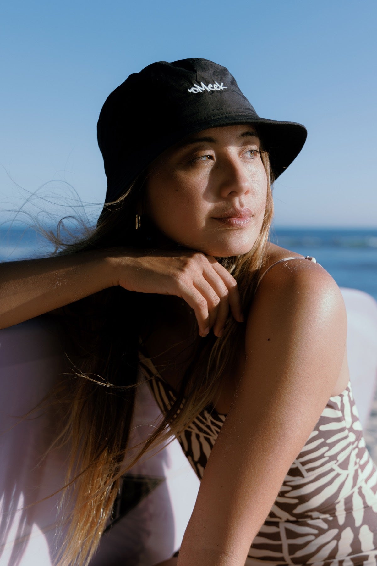 Woman in a black OMEEK bucket hat by the water.