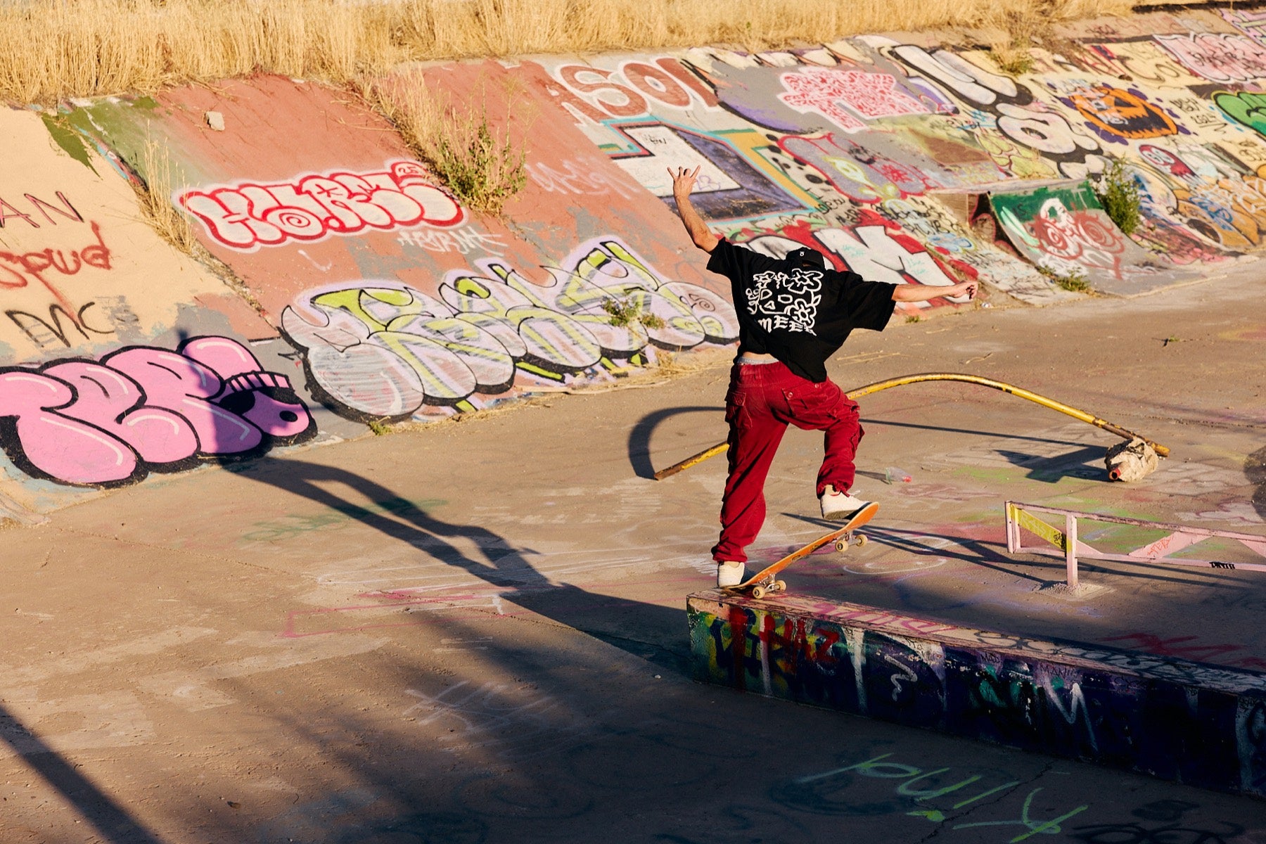 Skateboarder in a black graphic tee and red pants.