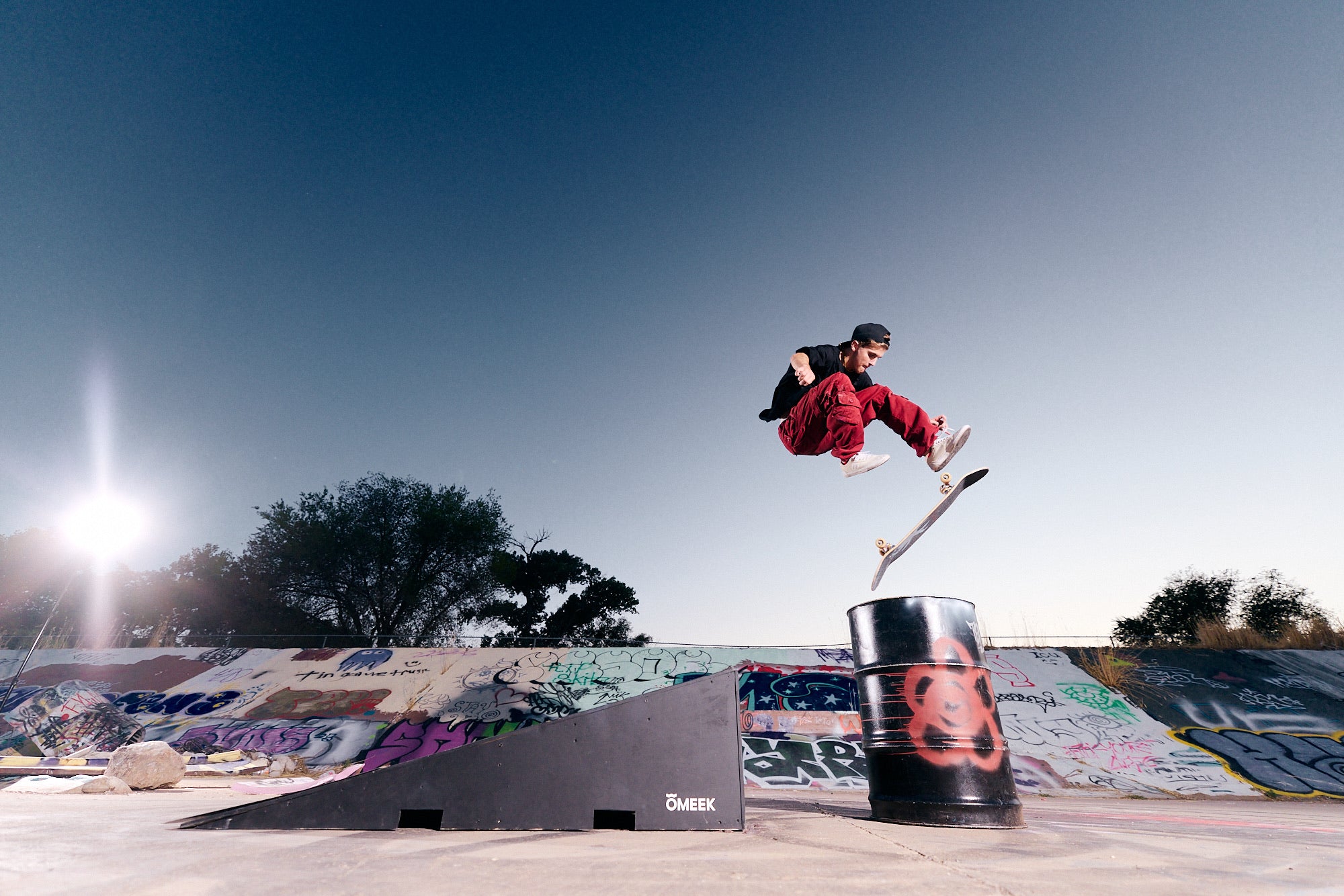 Parker DeMoux jumping a ramp toward a painted barrel at dusk.