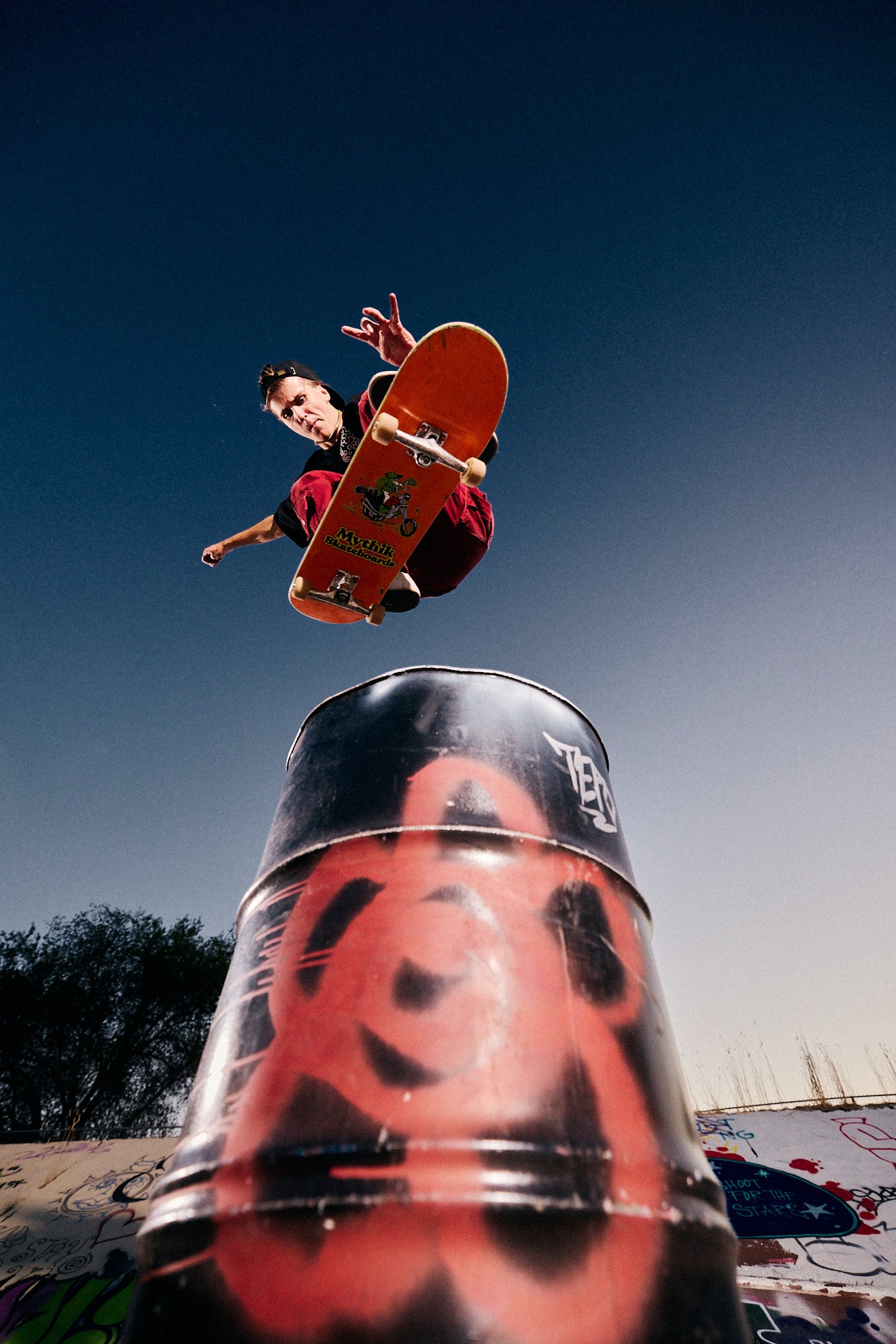 Skateboarder in midair above a painted barrel.