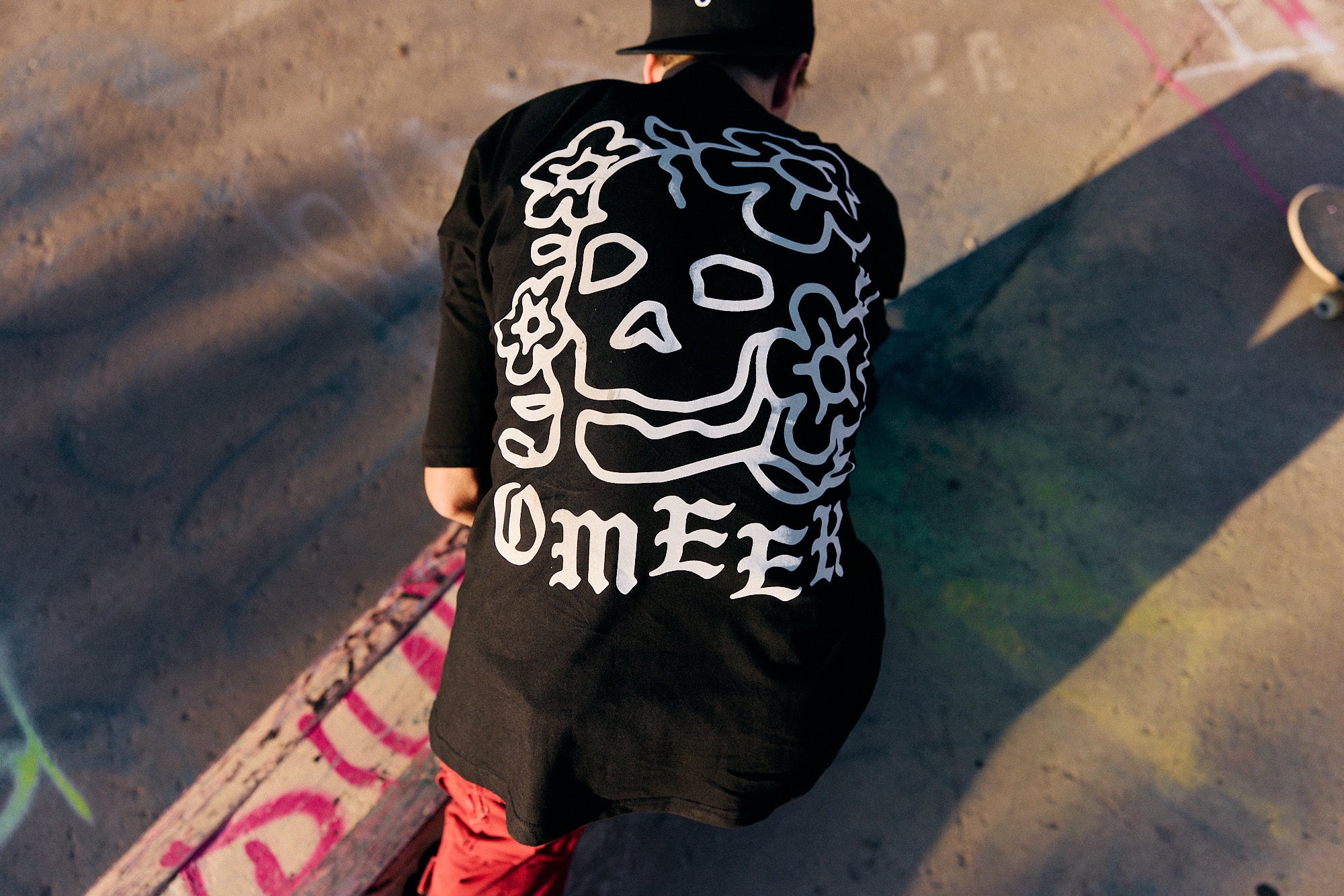 Skateboarder in a black OMEEK shirt with a white skull graphic, seen from above.