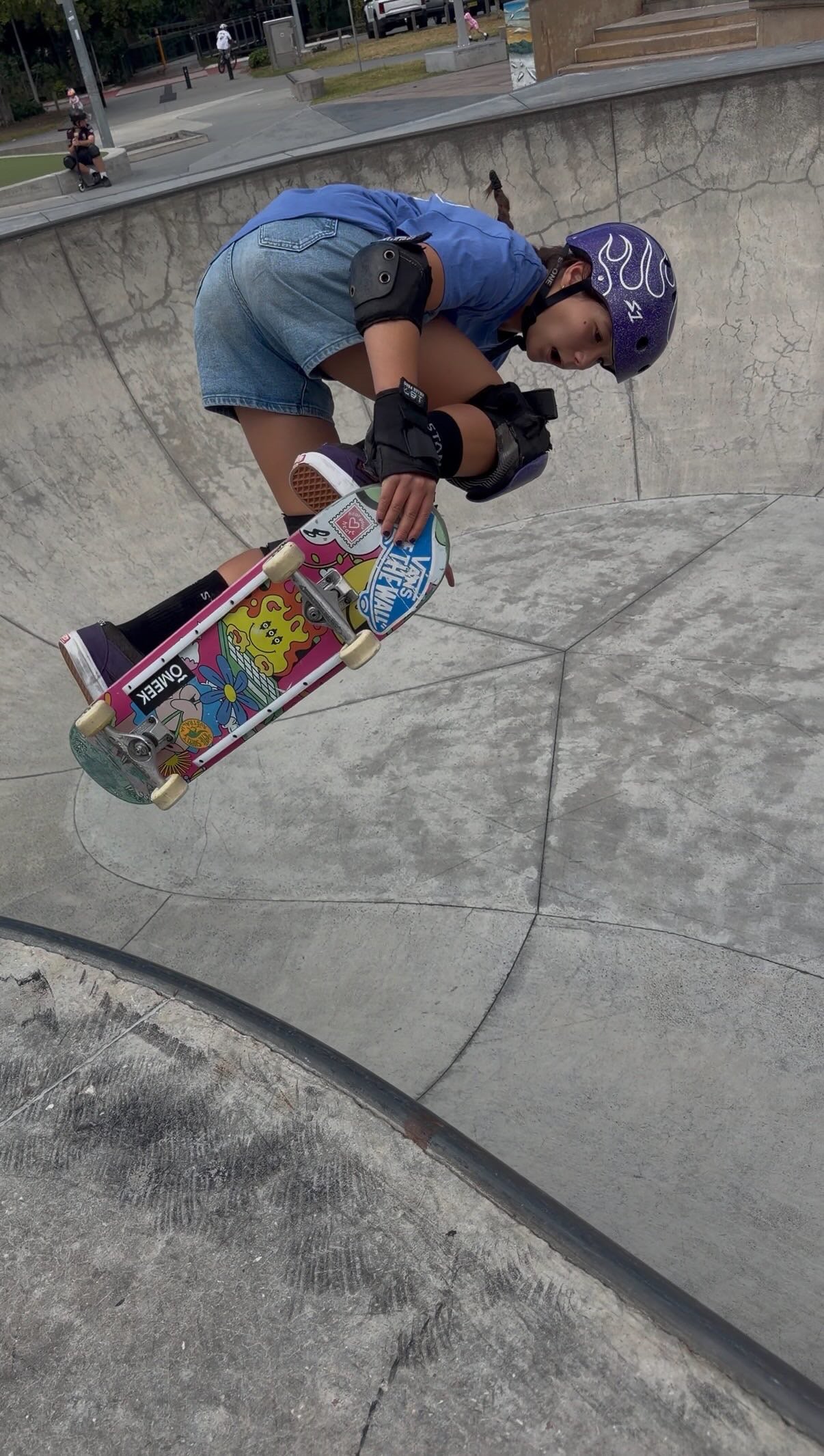 Ivy Raftery in a blue shirt and helmet holding a skateboard in a bowl.